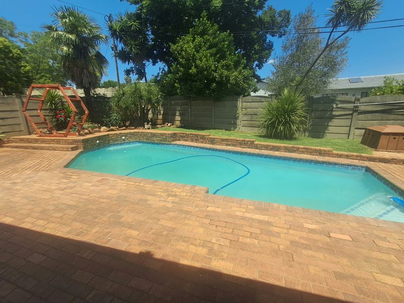 A well-maintained outdoor pool area featuring brick paving, a raised brick coping, and a secure perimeter wall in a landscaped garden setting.