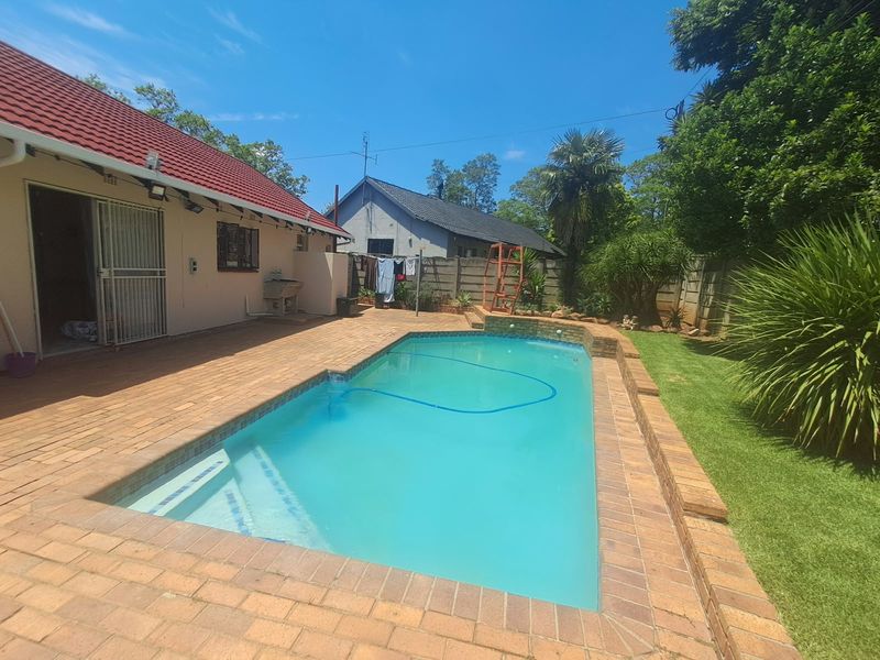 A well-maintained outdoor pool area featuring brick paving, a clear swimming pool, and a landscaped garden with a boundary wall.