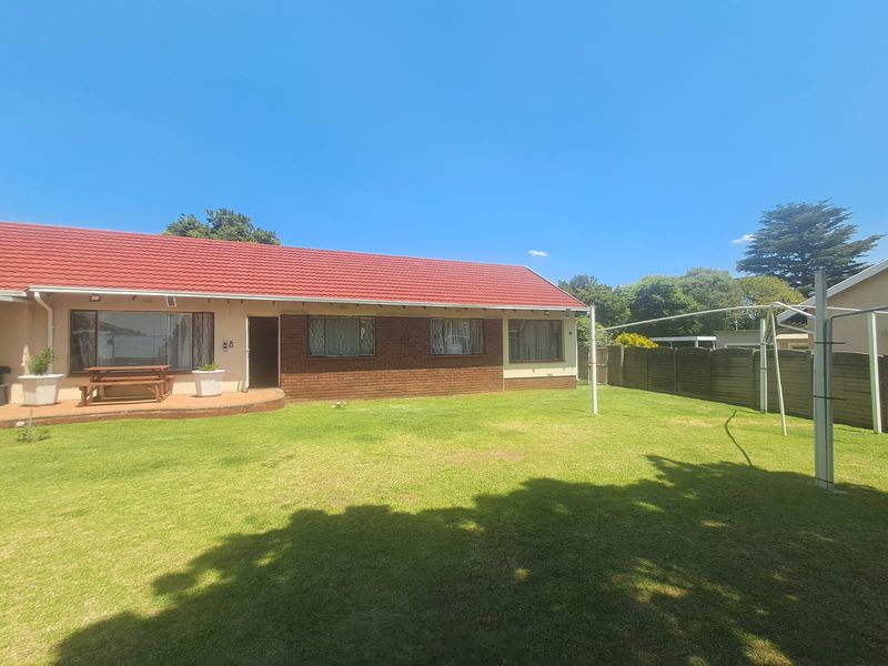 Rear view of the property featuring a spacious lawn, brick facade, red tiled roof, and a functional rotary clothesline.