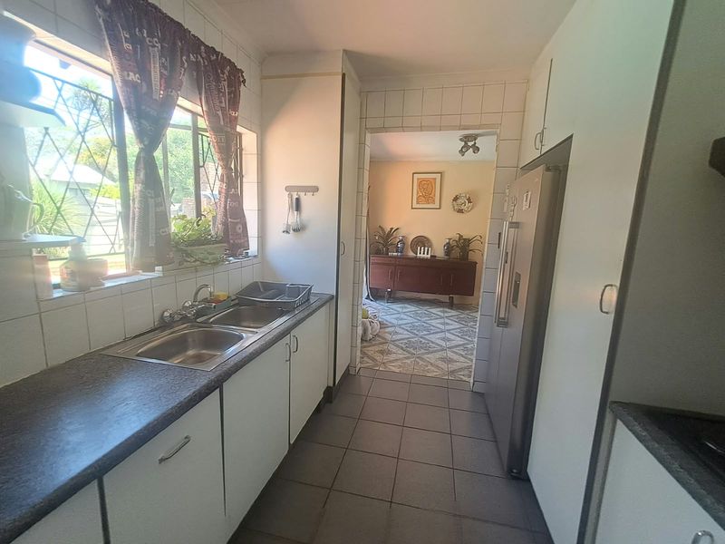 A functional kitchen featuring a double stainless steel sink, tiled splashbacks, and built-in cabinetry, with a view through to the adjacent living area.