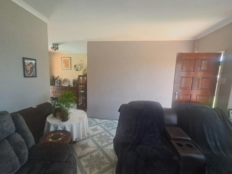 A living room area featuring tiled flooring, coved ceilings, and a traditional timber panel door leading to the exterior.