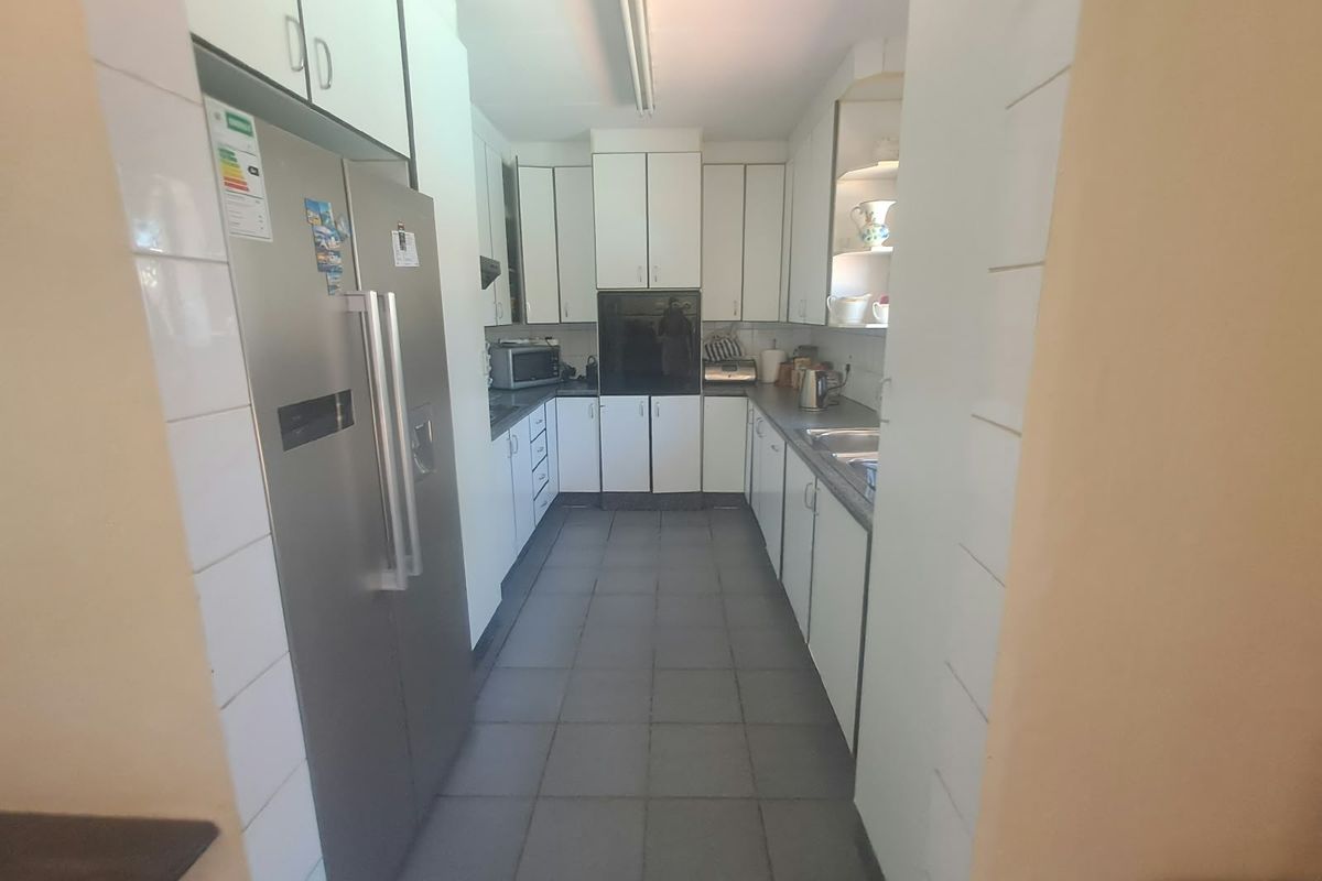 A functional galley-style kitchen featuring white cabinetry, tiled flooring, and integrated appliances, offering a clean and practical layout for daily meal preparation.