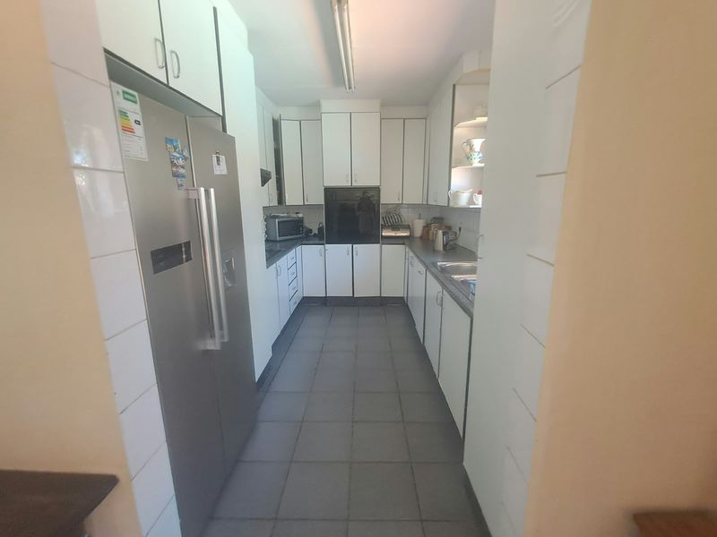 A functional galley-style kitchen featuring white cabinetry, tiled flooring, and integrated appliances, offering a clean and practical layout for daily meal preparation.