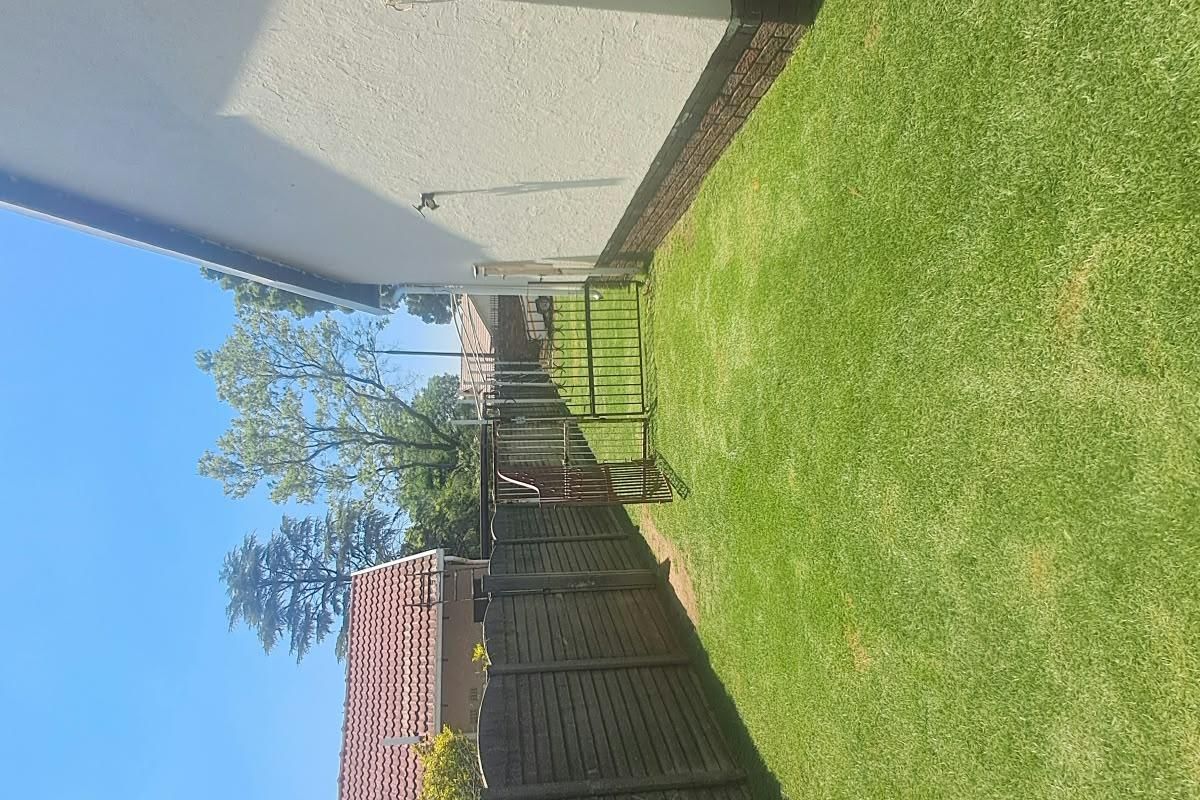 A side garden area featuring a well-maintained lawn, enclosed by a timber fence and a metal gate.