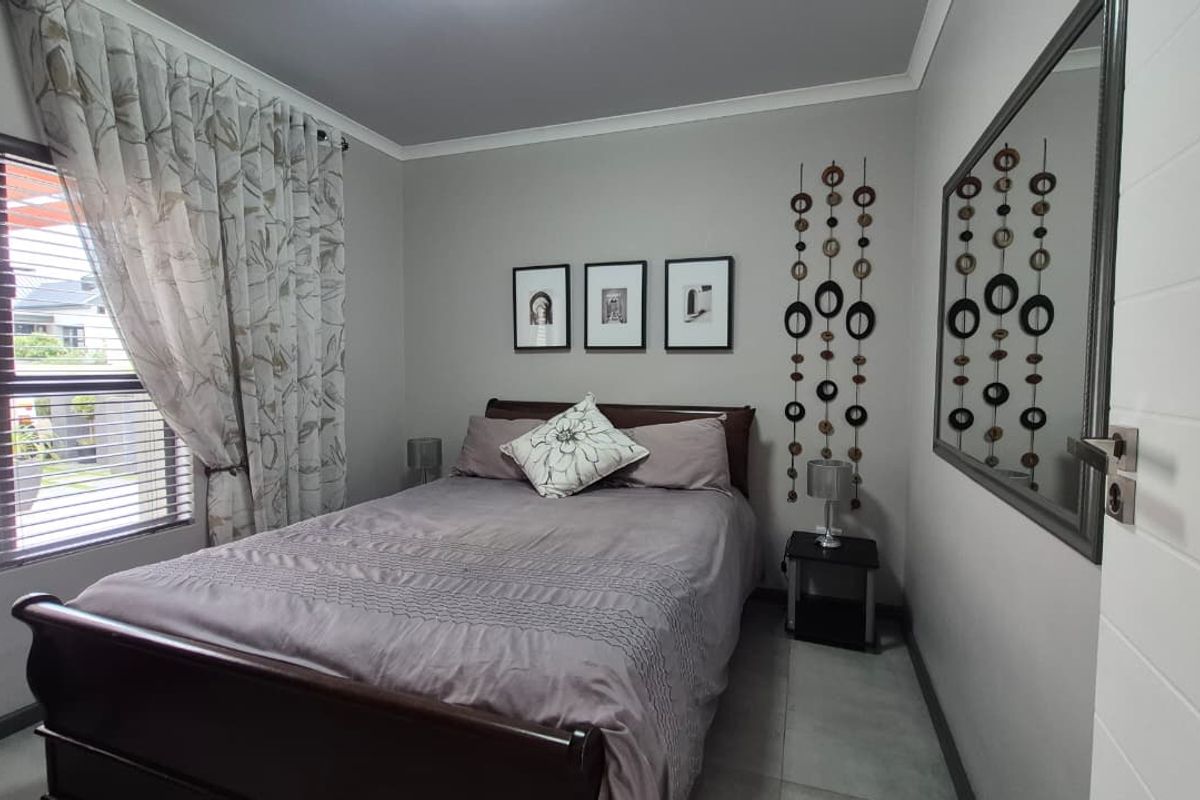 A well-maintained bedroom featuring neutral grey walls, tiled flooring, and a large window with blinds, providing a clean and comfortable living space.