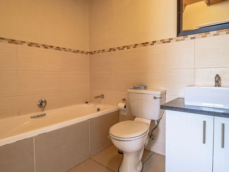 A functional bathroom featuring a built-in bathtub, a modern vessel sink on a vanity cabinet, and neutral wall tiling with a decorative border.