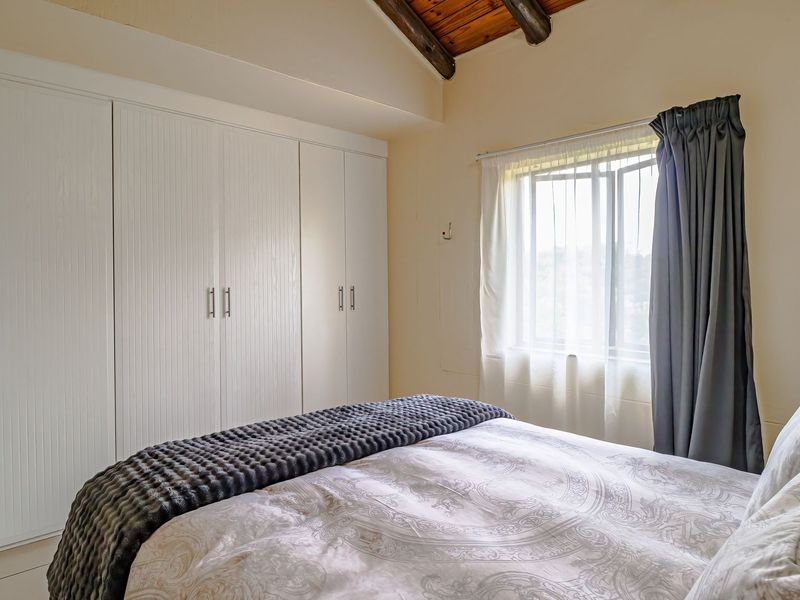 A well-maintained bedroom featuring built-in wardrobes, tiled flooring, and a vaulted ceiling with exposed timber beams.