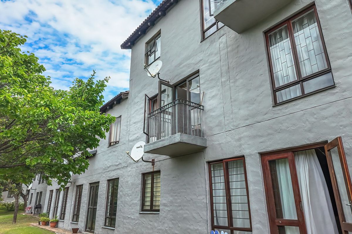 Rear elevation of a multi-story apartment building featuring a small balcony, timber-framed windows, and textured exterior walls set against a landscaped garden area.