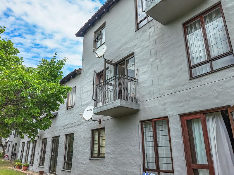 Rear elevation of a multi-story apartment building featuring a small balcony, timber-framed windows, and textured exterior walls set against a landscaped garden area.