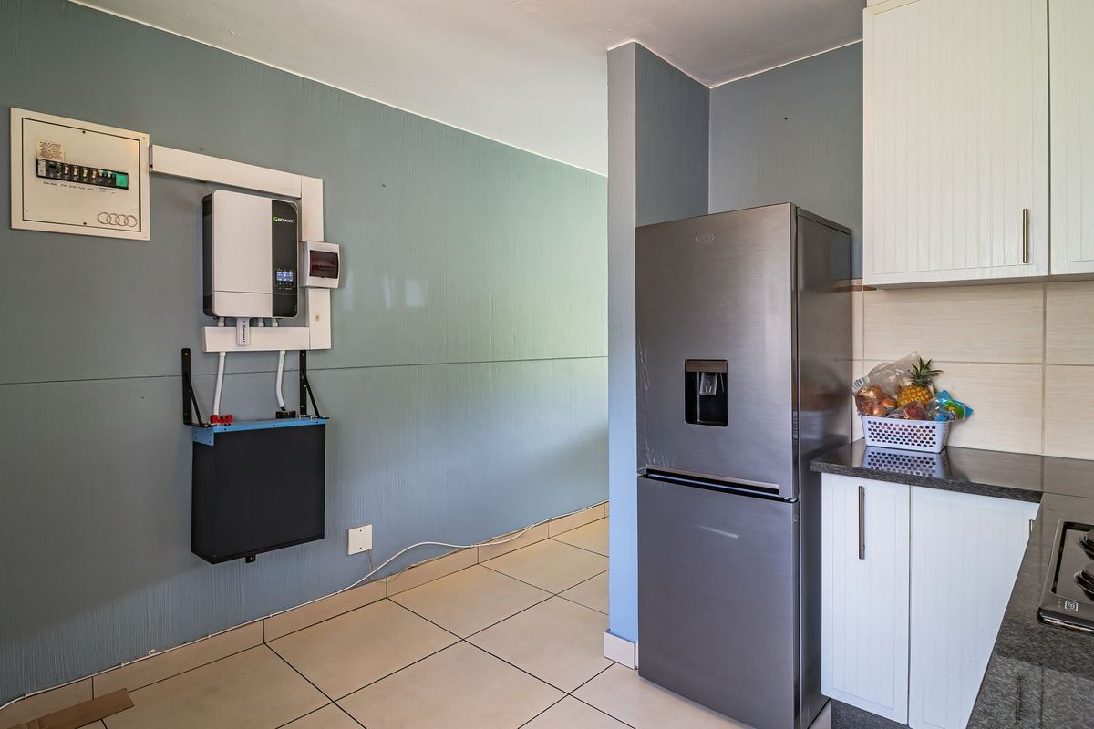 Kitchen area featuring built-in cabinetry, granite countertops, electric hob, and a wall-mounted solar inverter and battery backup system.