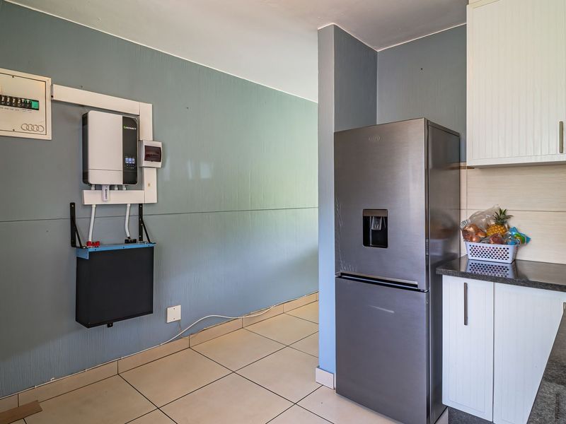 Kitchen area featuring built-in cabinetry, granite countertops, electric hob, and a wall-mounted solar inverter and battery backup system.