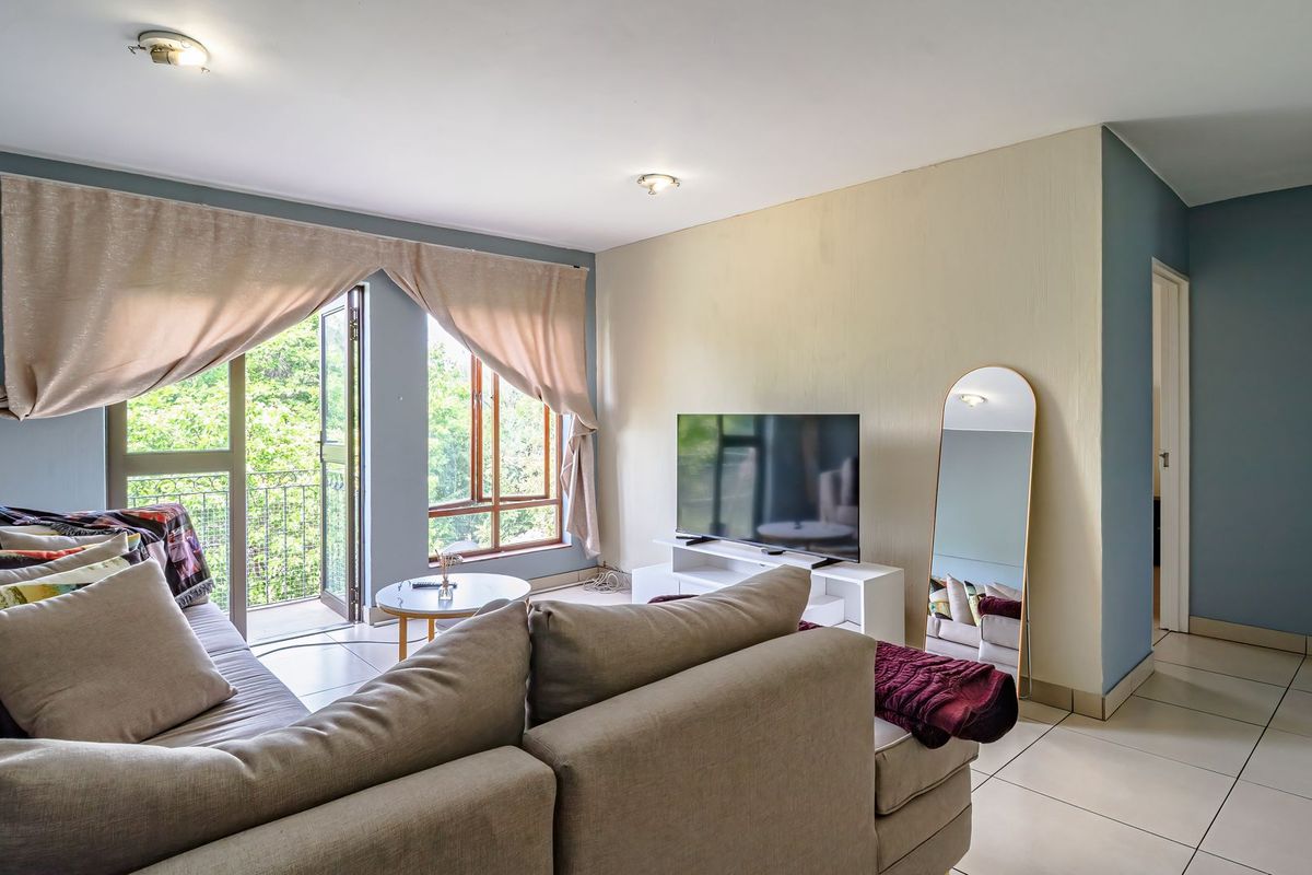 A bright living room featuring tiled flooring and direct access to a balcony through a glass door, offering natural light and outdoor views.