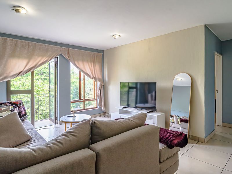 A bright living room featuring tiled flooring and direct access to a balcony through a glass door, offering natural light and outdoor views.