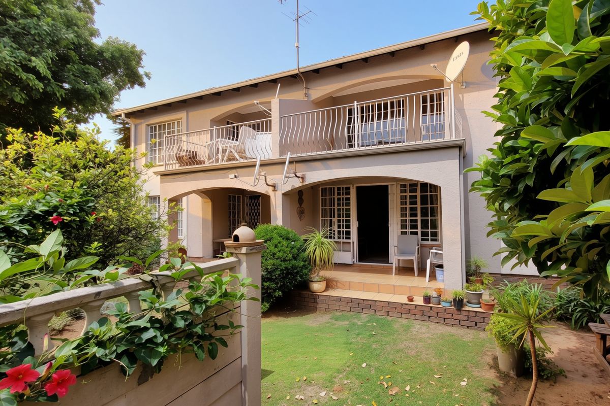 Rear view of a two-story townhouse featuring a ground-floor tiled patio, an upper-level balcony with metal railings, and a small private garden area.