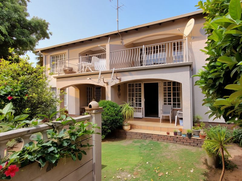 Rear view of a two-story townhouse featuring a ground-floor tiled patio, an upper-level balcony with metal railings, and a small private garden area.