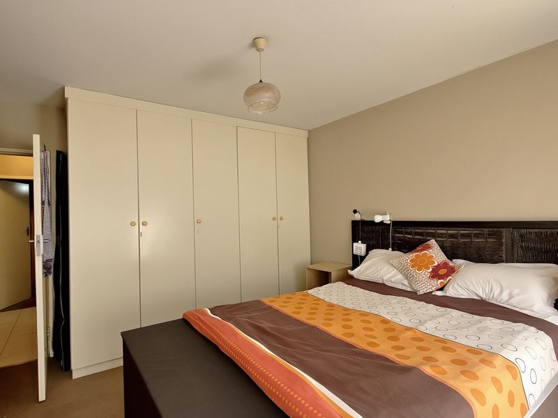A functional bedroom featuring ample built-in cupboard storage, neutral wall tones, and tiled flooring, providing a comfortable and practical living space.