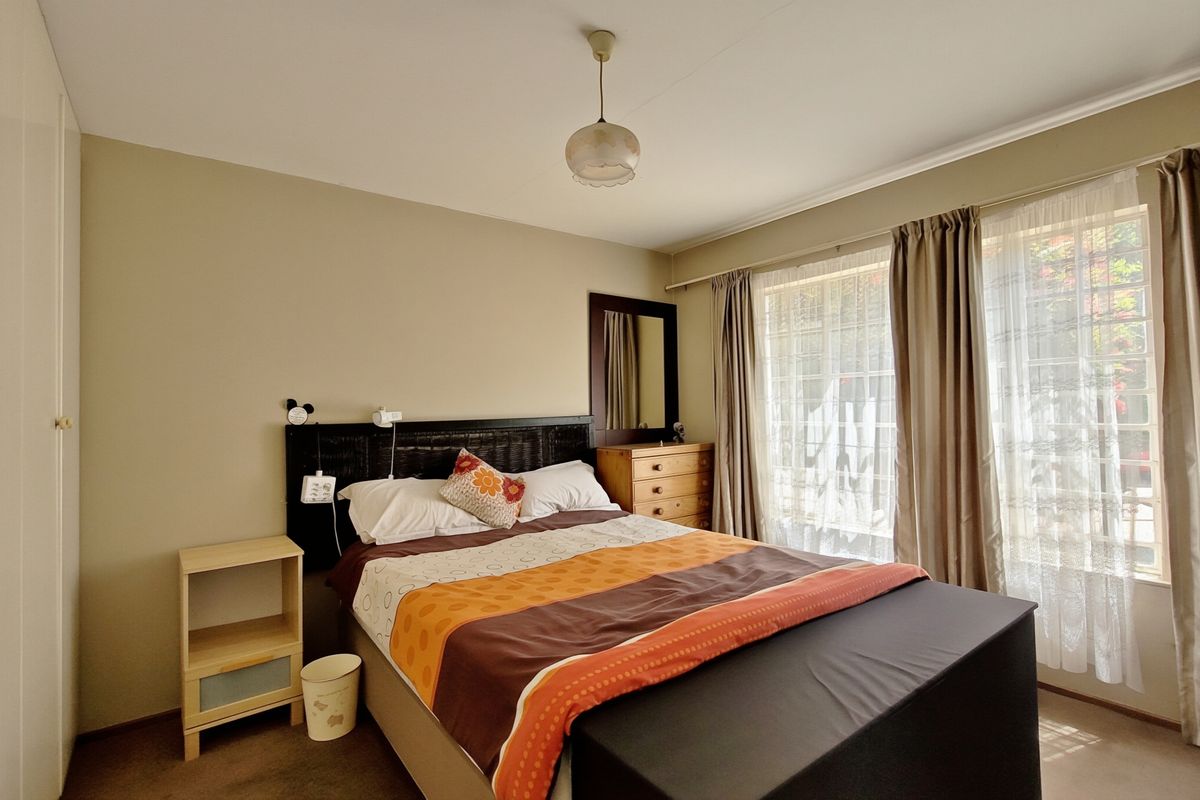 A well-lit bedroom featuring neutral wall tones, carpeted flooring, and a built-in wardrobe, offering a comfortable and functional living space.
