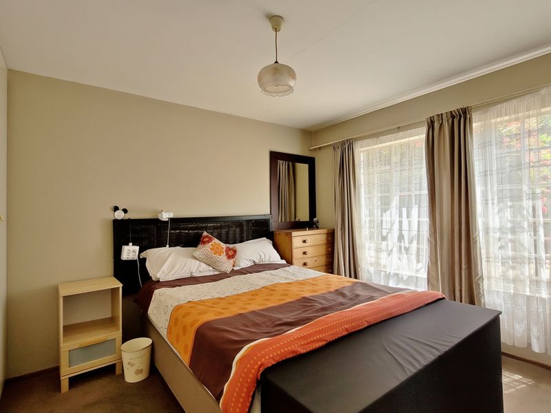 A well-lit bedroom featuring neutral wall tones, carpeted flooring, and a built-in wardrobe, offering a comfortable and functional living space.