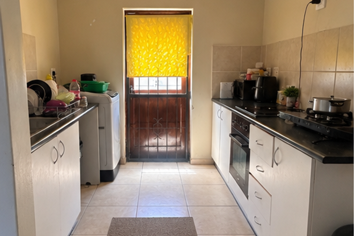 Functional galley-style kitchen featuring built-in cabinetry, oven, hob, and tiled finishes with direct access to the exterior via a security gate.