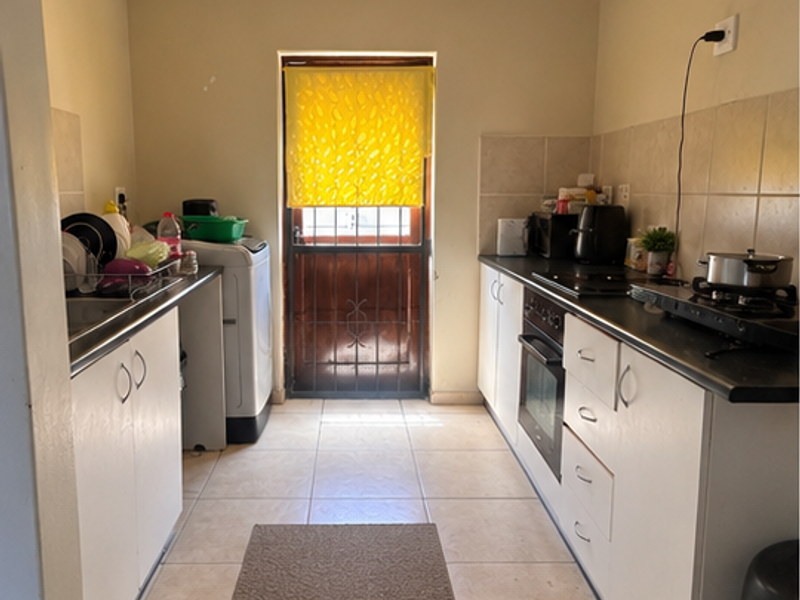 Functional galley-style kitchen featuring built-in cabinetry, oven, hob, and tiled finishes with direct access to the exterior via a security gate.