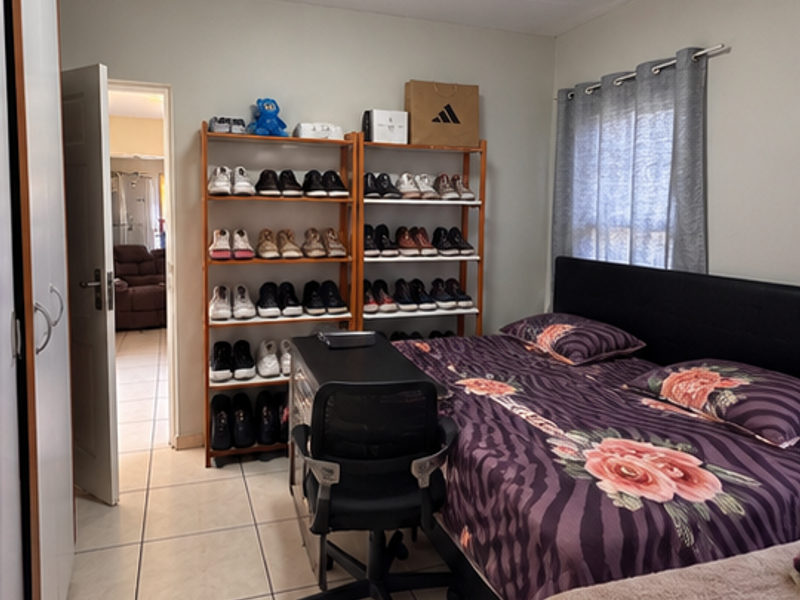 A functional bedroom featuring tiled flooring, a built-in wardrobe, and a window with a curtain rod, offering a practical living space.