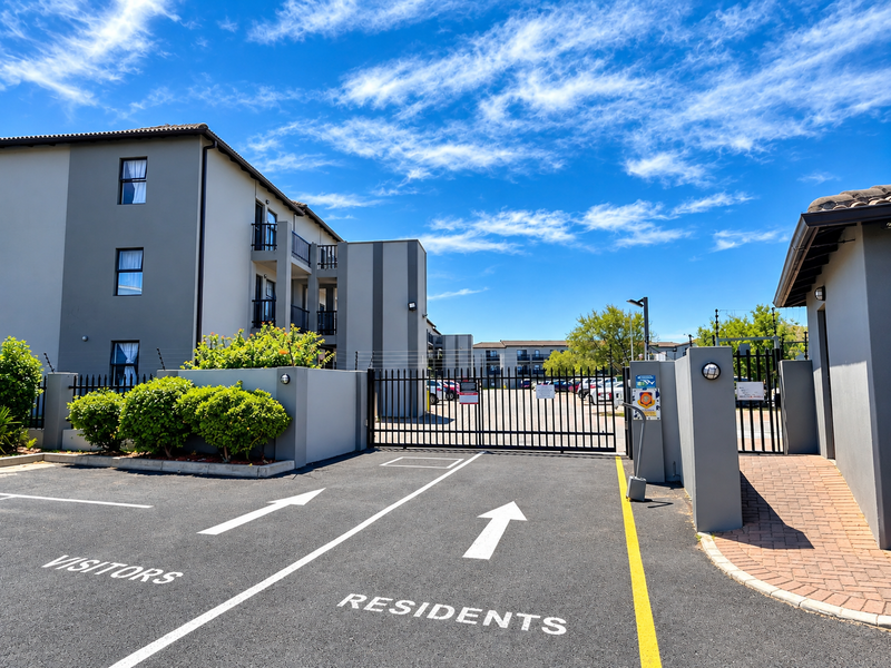 The entrance to the townhouse complex features a secure gated access point with designated visitor and resident lanes, electric fencing, and modern exterior finishes.