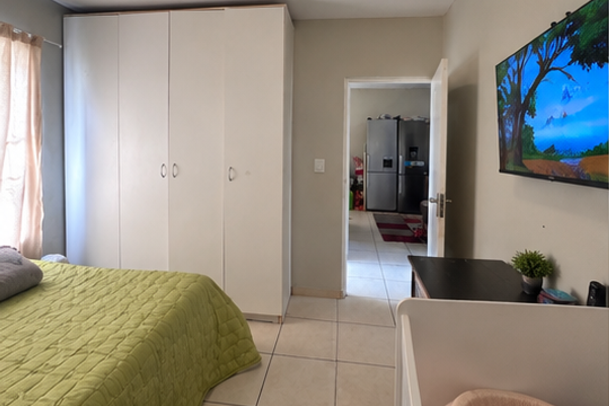 A bedroom featuring tiled flooring and a large built-in wardrobe, with a doorway leading to an adjacent kitchen area.