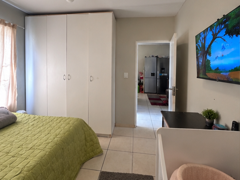 A bedroom featuring tiled flooring and a large built-in wardrobe, with a doorway leading to an adjacent kitchen area.