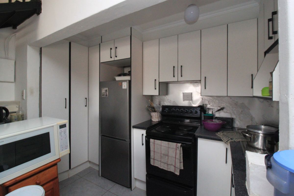 A functional kitchen featuring white built-in cabinetry, dark laminate countertops, a stainless steel splashback, and a freestanding stove.