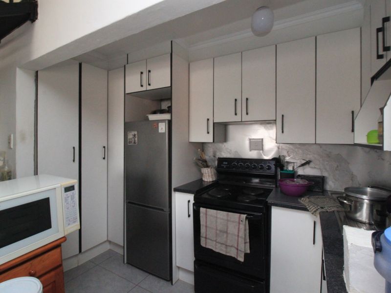A functional kitchen featuring white built-in cabinetry, dark laminate countertops, a stainless steel splashback, and a freestanding stove.