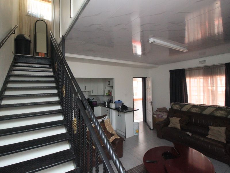 Open plan living area featuring a metal staircase with wrought iron railing, tiled flooring, and a compact kitchen with built-in cabinetry.
