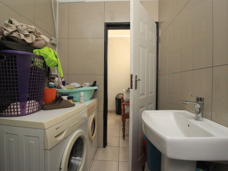 A functional laundry room featuring tiled walls and flooring, a pedestal basin with a mixer tap, and space for a washing machine.