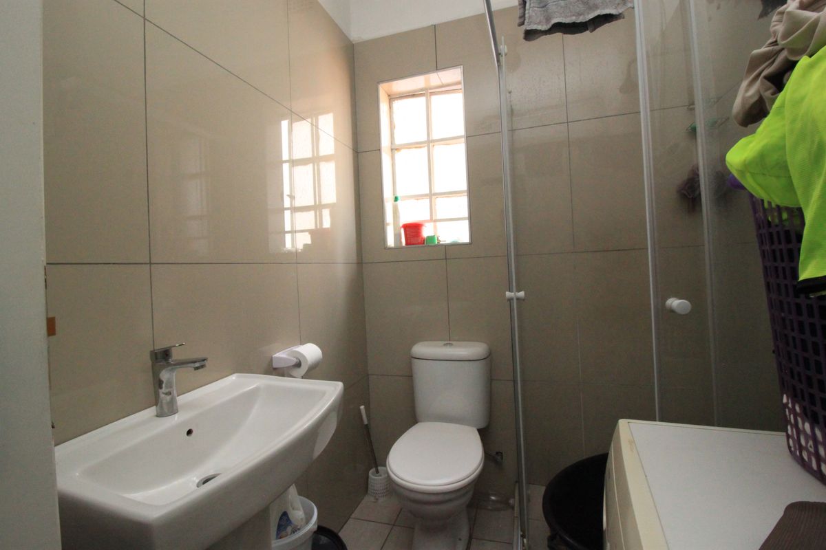 A compact bathroom featuring neutral wall tiles, a pedestal basin with chrome mixer tap, a standard toilet, and a glass shower screen.