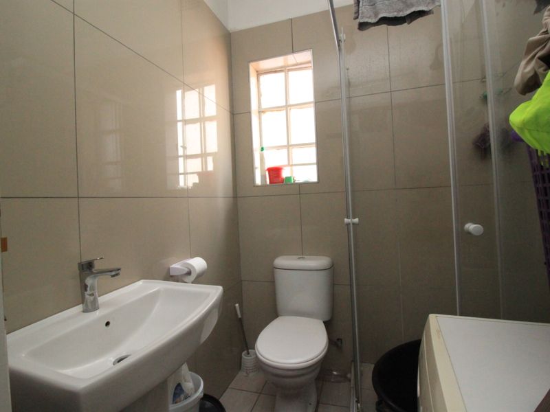 A compact bathroom featuring neutral wall tiles, a pedestal basin with chrome mixer tap, a standard toilet, and a glass shower screen.