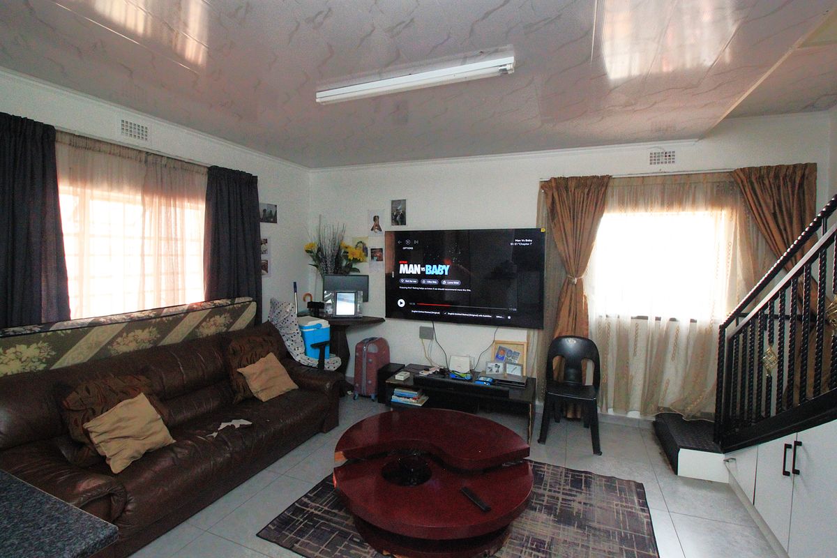 A living room area featuring tiled flooring, a staircase, and a wall-mounted television, providing a functional space for relaxation.