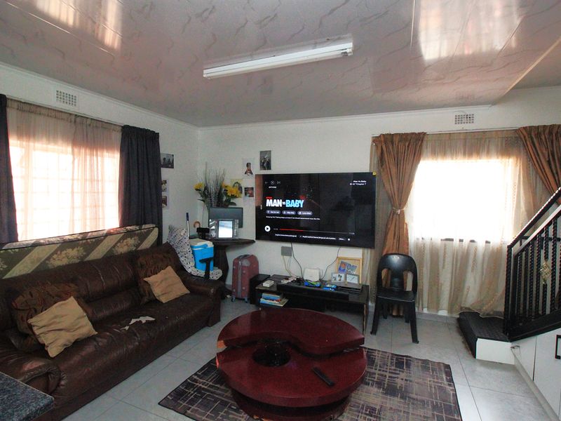 A living room area featuring tiled flooring, a staircase, and a wall-mounted television, providing a functional space for relaxation.