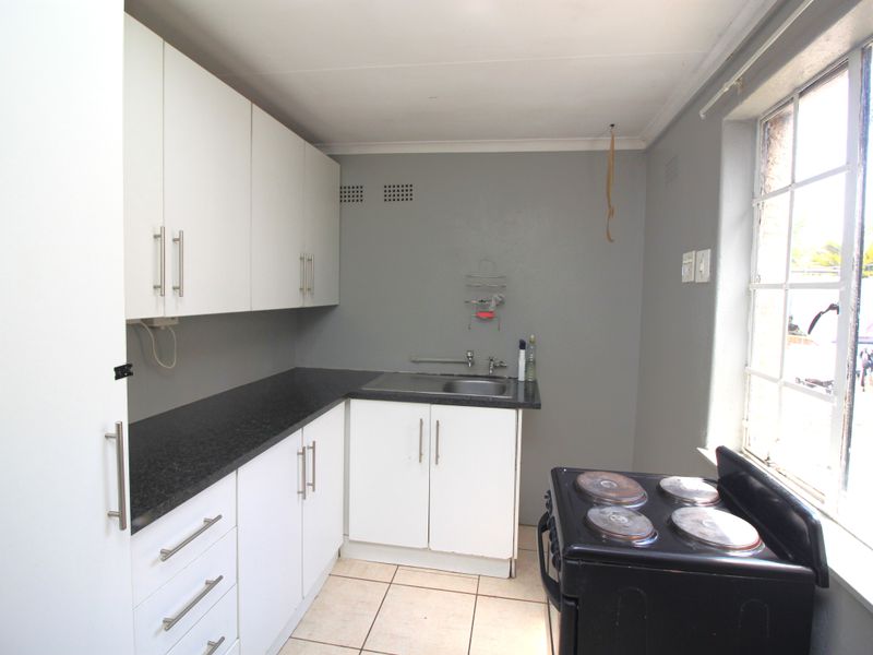 Compact kitchen featuring white cabinetry, dark laminate countertops, tiled flooring, and a window providing natural light.