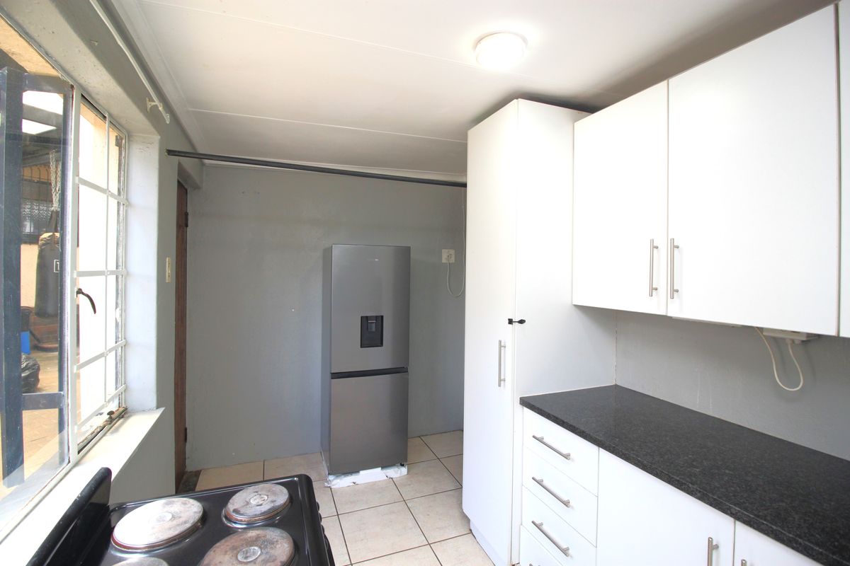 A functional kitchen featuring white cabinetry, dark countertops, tiled flooring, and an electric stove, offering a practical layout for daily meal preparation.