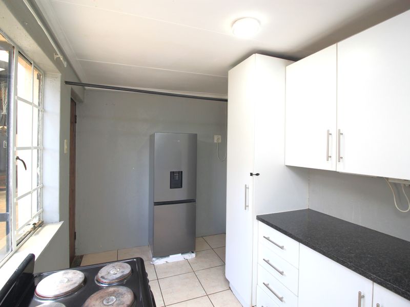 A functional kitchen featuring white cabinetry, dark countertops, tiled flooring, and an electric stove, offering a practical layout for daily meal preparation.
