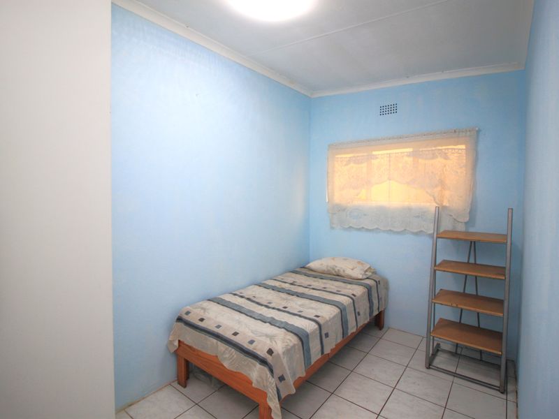 A compact bedroom featuring light blue walls, tiled flooring, and a built-in cupboard, offering a functional space with potential for modernization.