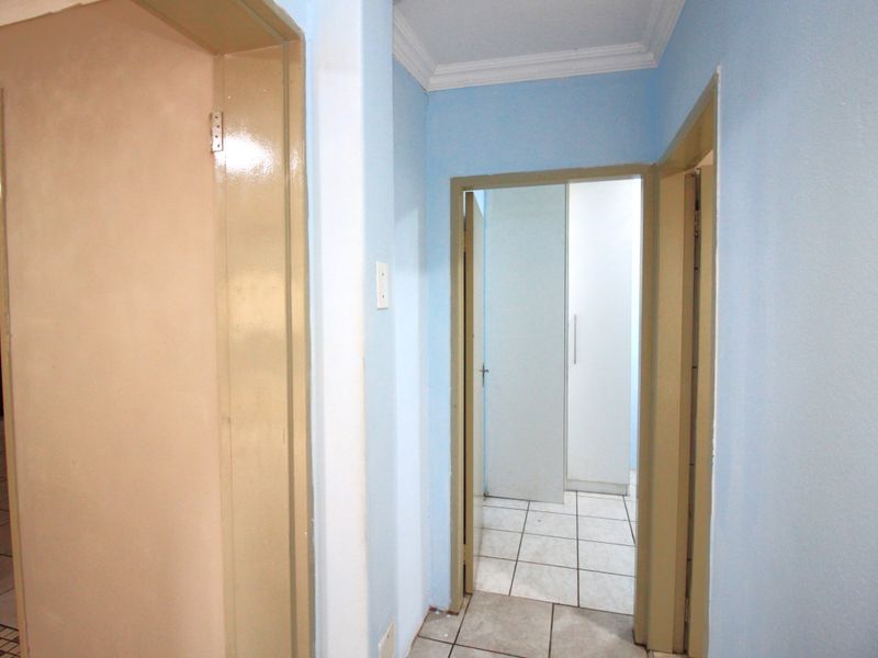 A functional hallway featuring tiled flooring, built-in cupboards, and access to adjacent rooms, finished with simple cornicing.