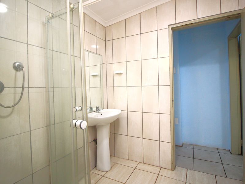 A functional bathroom featuring a pedestal basin, a glass-enclosed shower, and neutral wall and floor tiling throughout.