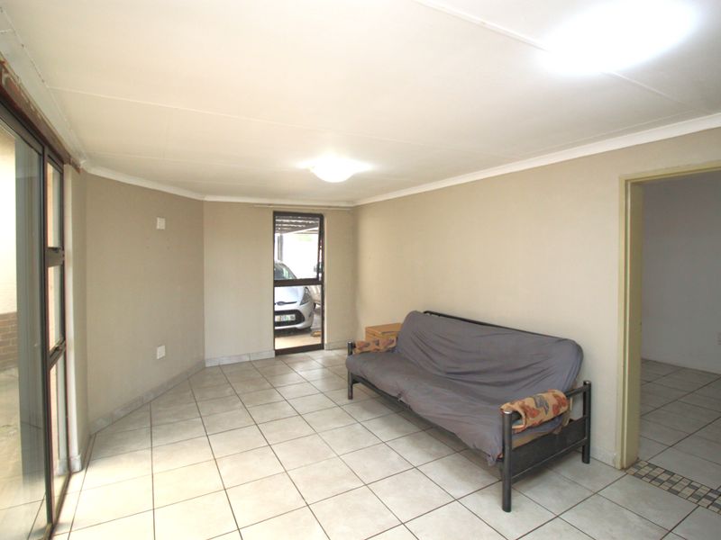 A functional living area featuring neutral tiled flooring, coved ceilings, and a sliding glass door providing access to the exterior.
