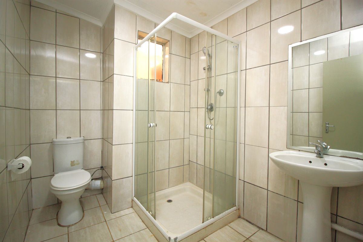 A functional bathroom featuring a shower enclosure, pedestal basin, and toilet with full-height wall tiling and neutral floor tiles.