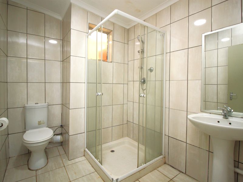 A functional bathroom featuring a shower enclosure, pedestal basin, and toilet with full-height wall tiling and neutral floor tiles.