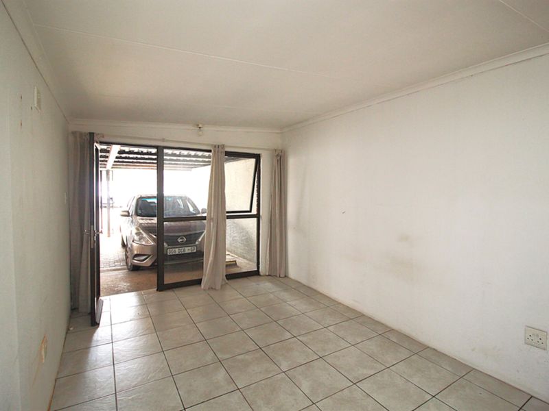 An empty living room featuring tiled flooring and a sliding glass door providing access to the exterior parking area.