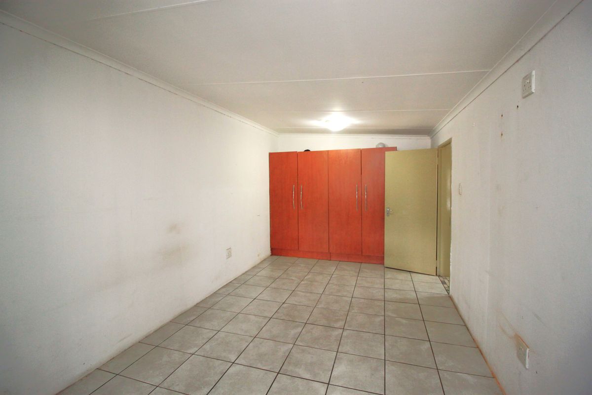 An empty bedroom featuring tiled flooring, built-in wooden cupboards, and coved ceilings, requiring minor cosmetic updates to the wall finishes.