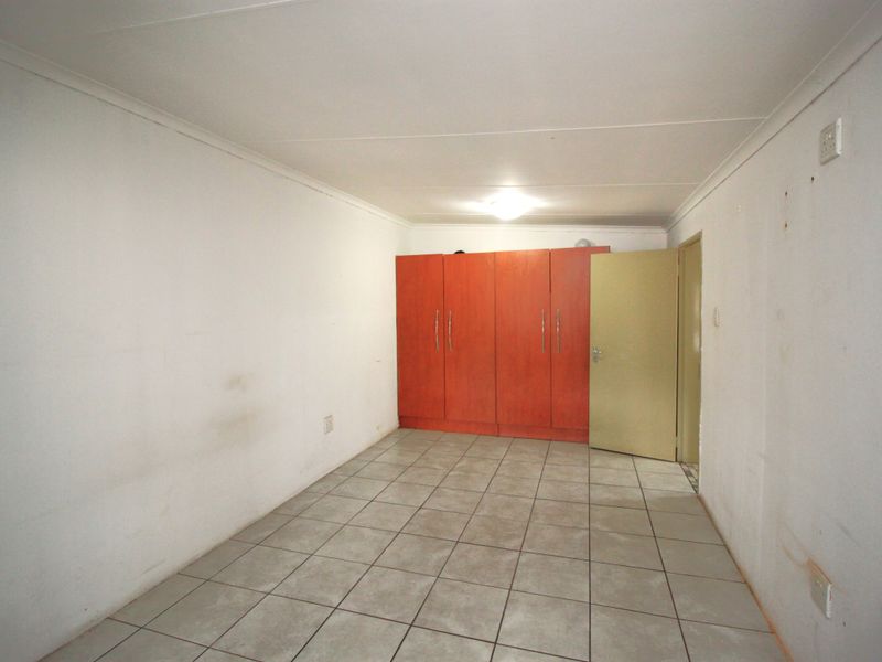 An empty bedroom featuring tiled flooring, built-in wooden cupboards, and coved ceilings, requiring minor cosmetic updates to the wall finishes.