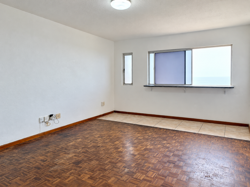 An empty living area featuring a combination of parquet and ceramic tile flooring, with a window sill and ocean view.