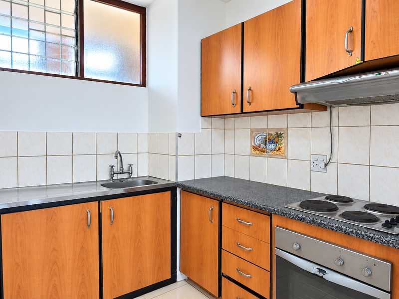 A functional kitchen featuring wood-look laminate cabinetry, a stainless steel sink, built-in oven with electric hob, and a tiled backsplash.